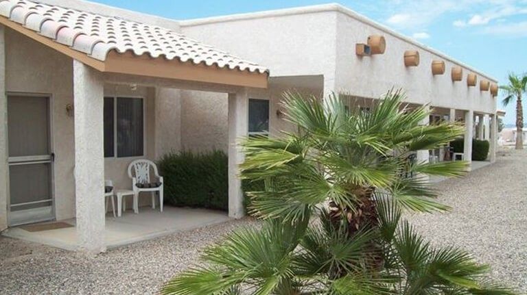 A residential house with a porch and palm tree in an arid climate setting.
