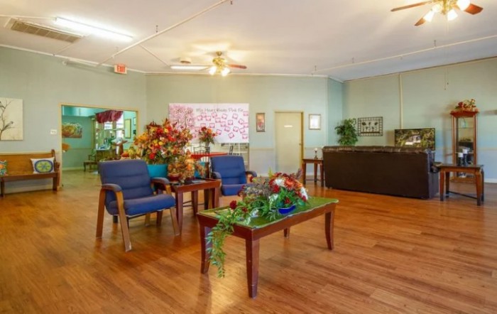 A cozy living room with comfortable chairs and vibrant floral arrangements on wooden flooring.
