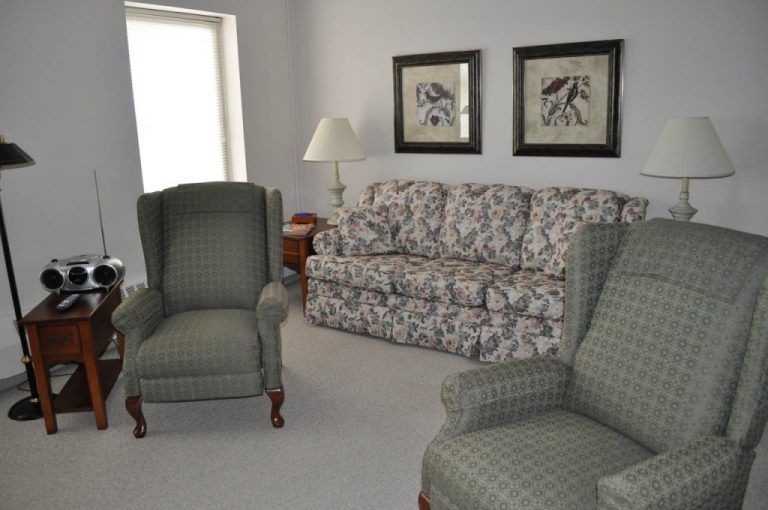 A cozy living room with a floral sofa, two plaid armchairs, and decorative artwork on the wall.