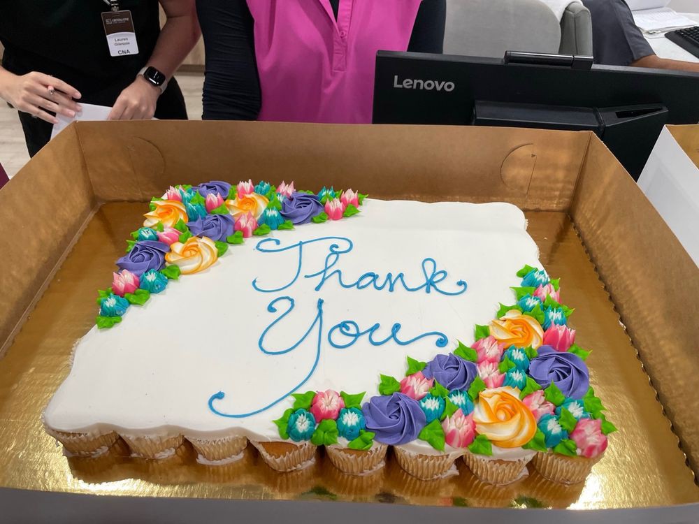 A beautifully decorated cake with 'Thank You' written in icing, adorned with colorful floral designs.