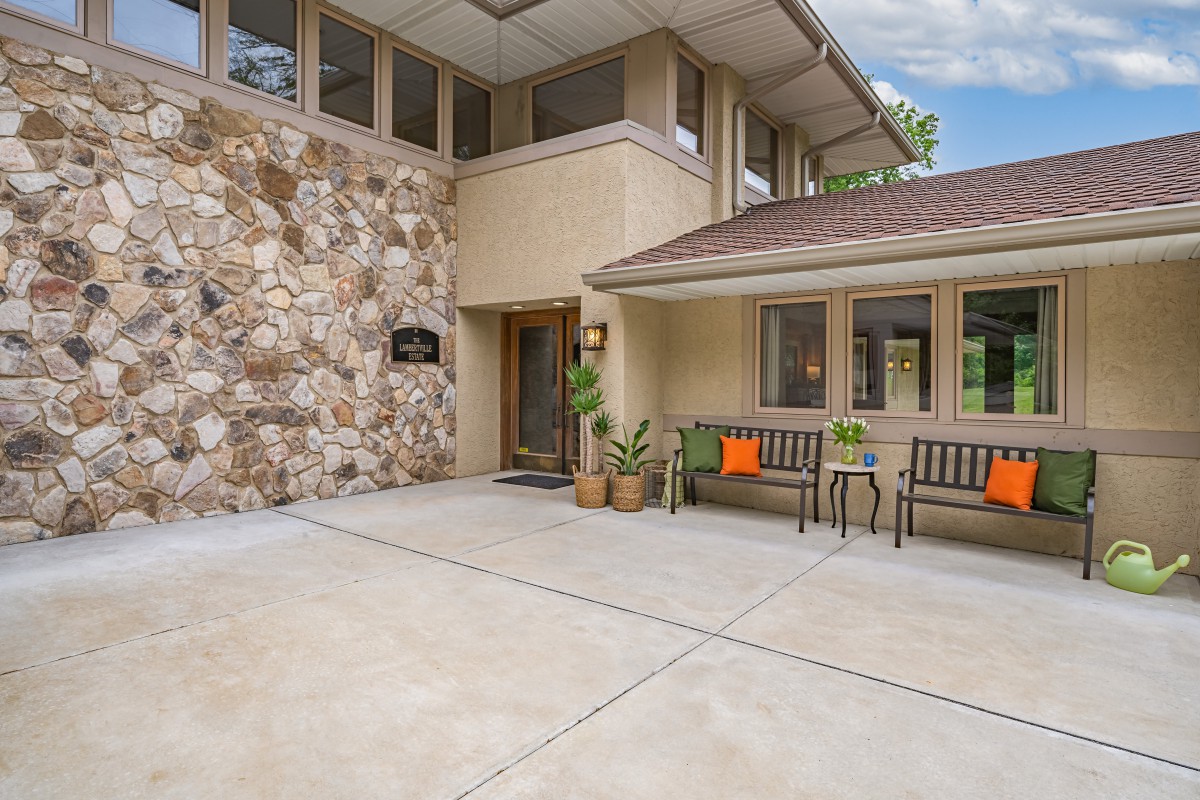 A modern home entrance with stone wall accents, benches, and potted plants.