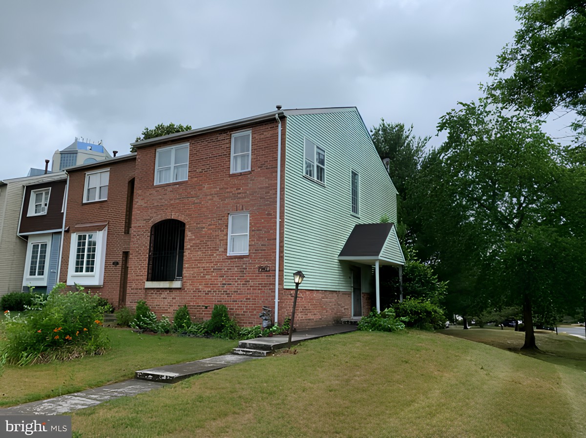 A two-story brick and siding house with a front lawn and surrounding trees under a cloudy sky.