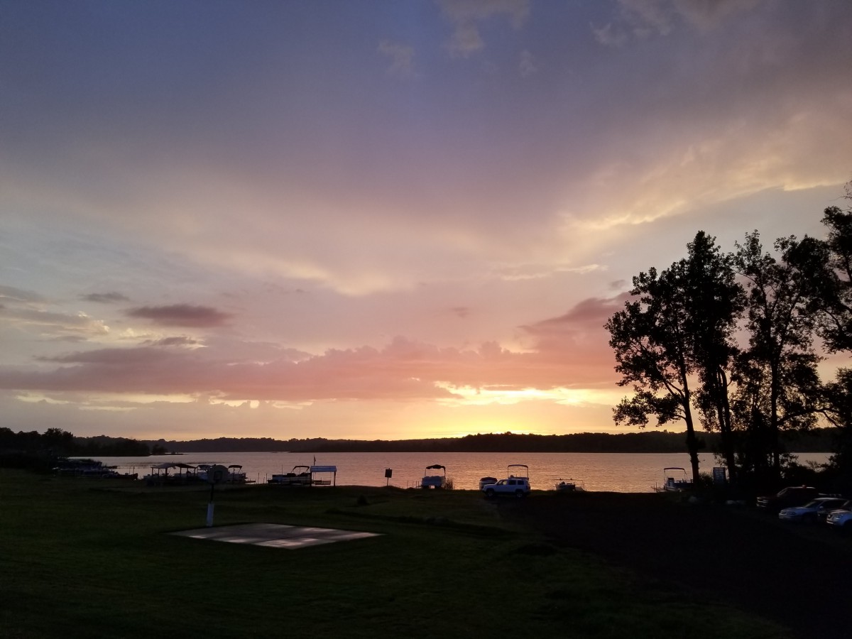 A serene sunset over a tranquil lake with silhouetted trees and colorful clouds.