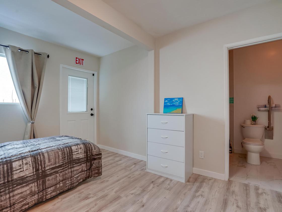 A minimalist bedroom featuring a bed, dresser, and light wood flooring.