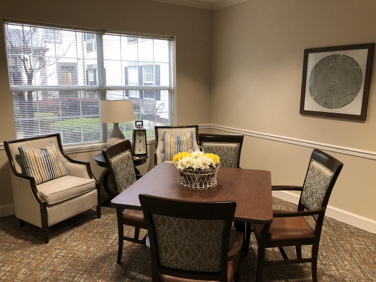 A cozy dining area with a wooden table, surrounding chairs, a lamp by the window, and artwork on the wall.