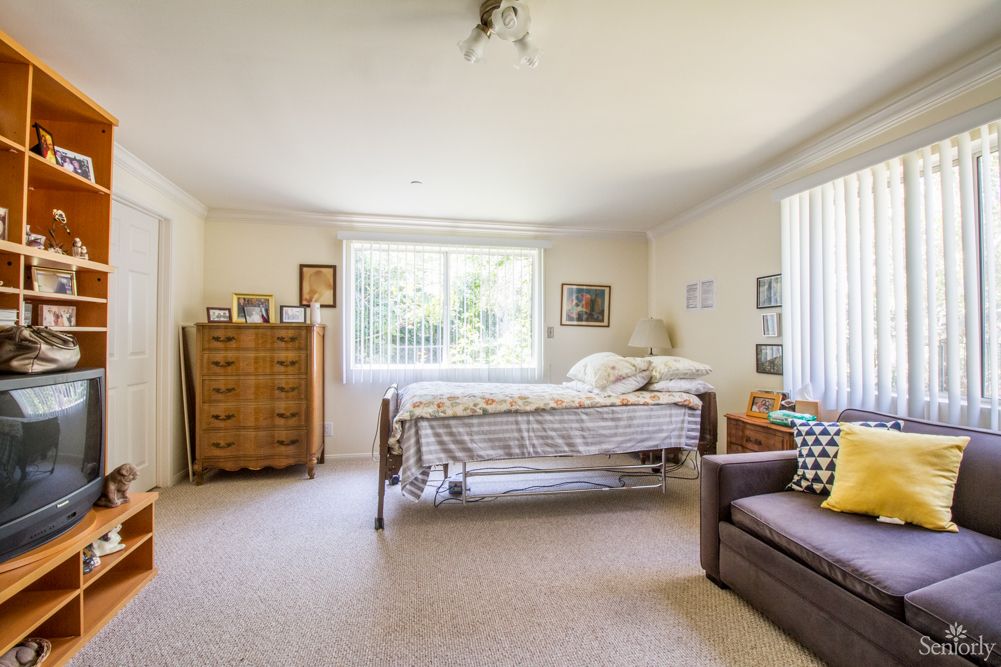 A cozy bedroom with a bed, dresser, and large windows allowing natural light.