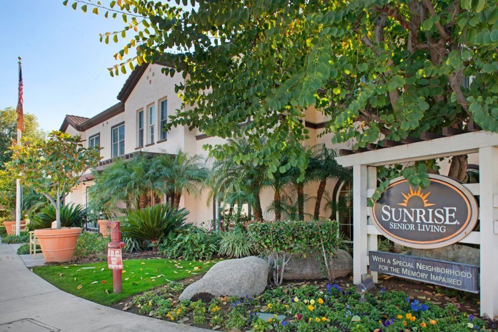 A picturesque building surrounded by lush greenery and vibrant flowers, with a visible sign in front.