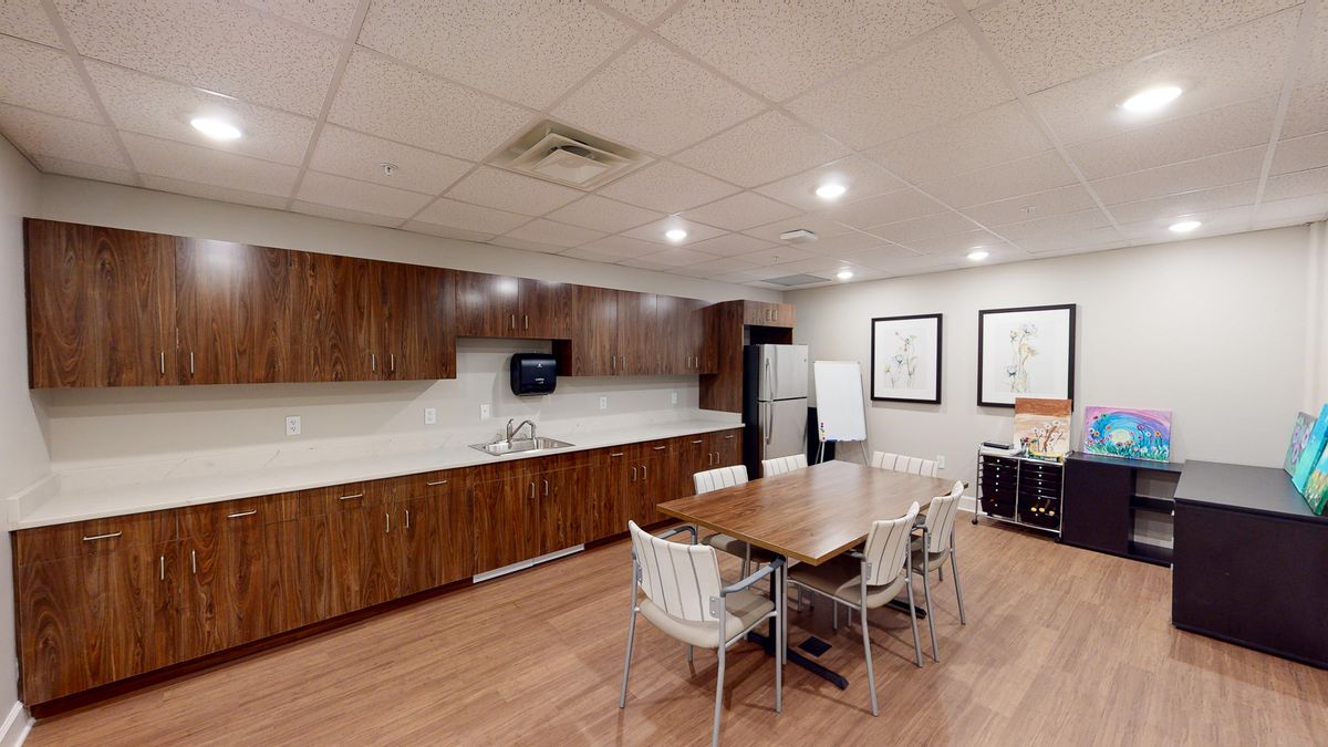 A modern office kitchen and break room with wooden cabinets, a central table, and various appliances.
