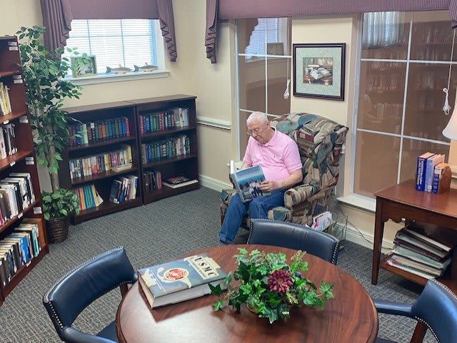 A person reading a book in a cozy library setting with bookshelves and comfortable seating.