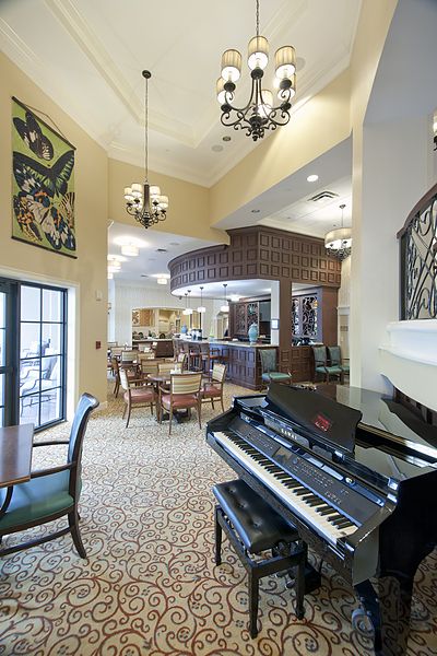 A stylish lounge area featuring a grand piano, elegant chandeliers, and arranged dining tables, creating a cozy and inviting atmosphere.