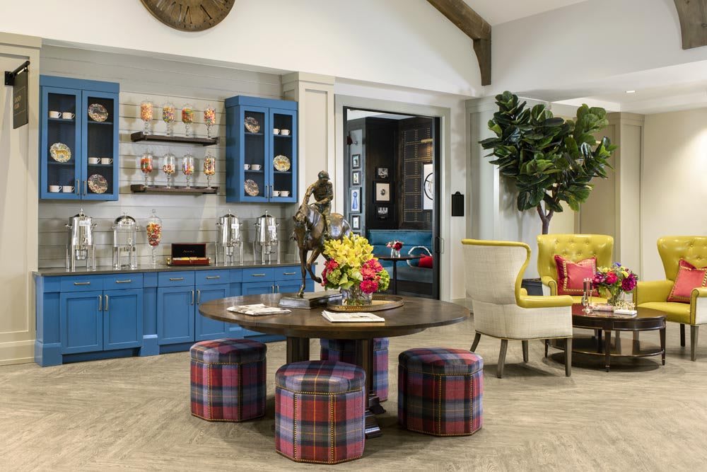 A vibrant living room with colorful furniture and decor, featuring a round table surrounded by plaid stools and a bright flower arrangement.