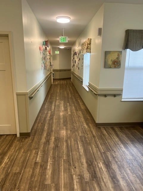 A brightly lit hallway with wooden flooring and handrails along the walls.