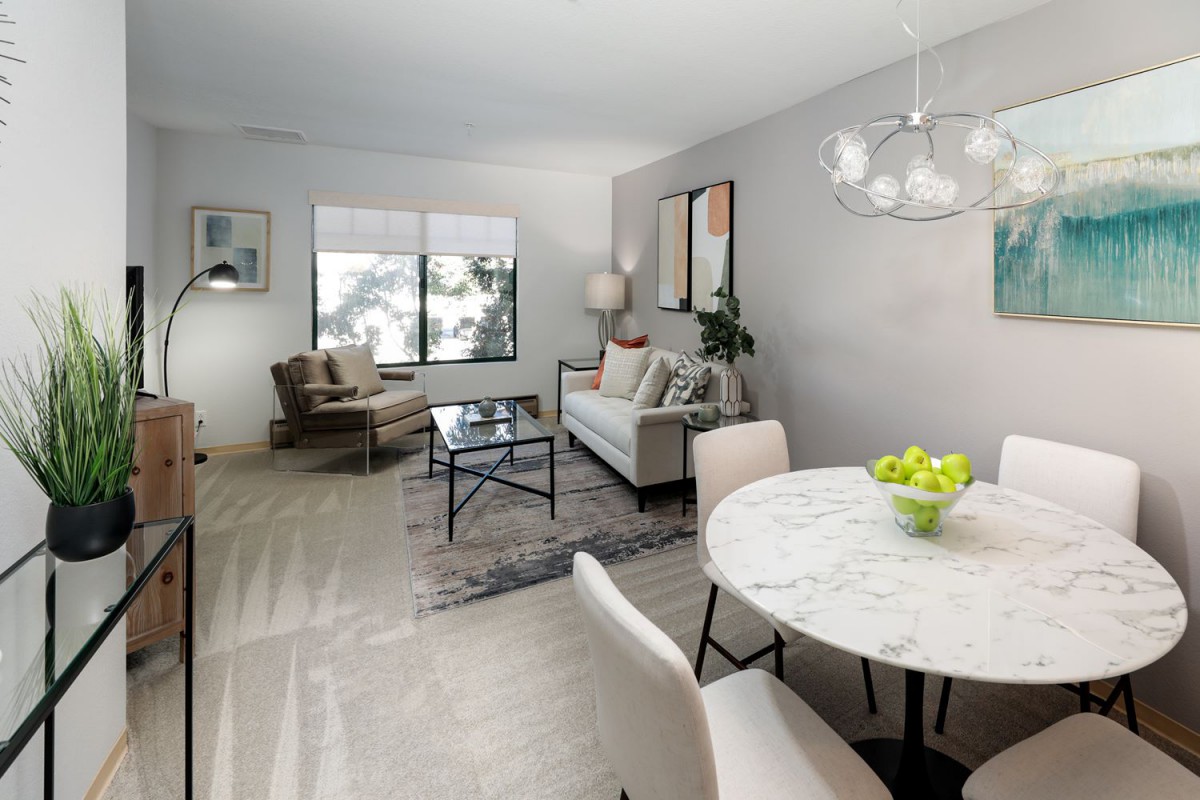 A modern living room with minimalist decor featuring a sofa, armchairs, and a dining table in light neutral tones.