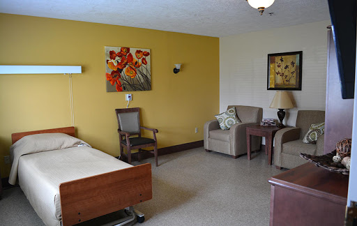 A well-furnished hospital room featuring a bed, comfortable chairs, and decorative artwork on the walls.