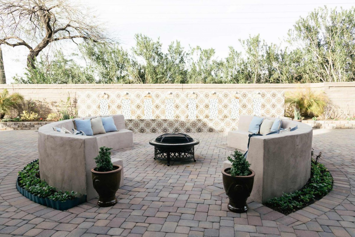 A cozy patio with comfortable seating around a fire pit, adorned with potted plants and enclosed by a decorative wall.