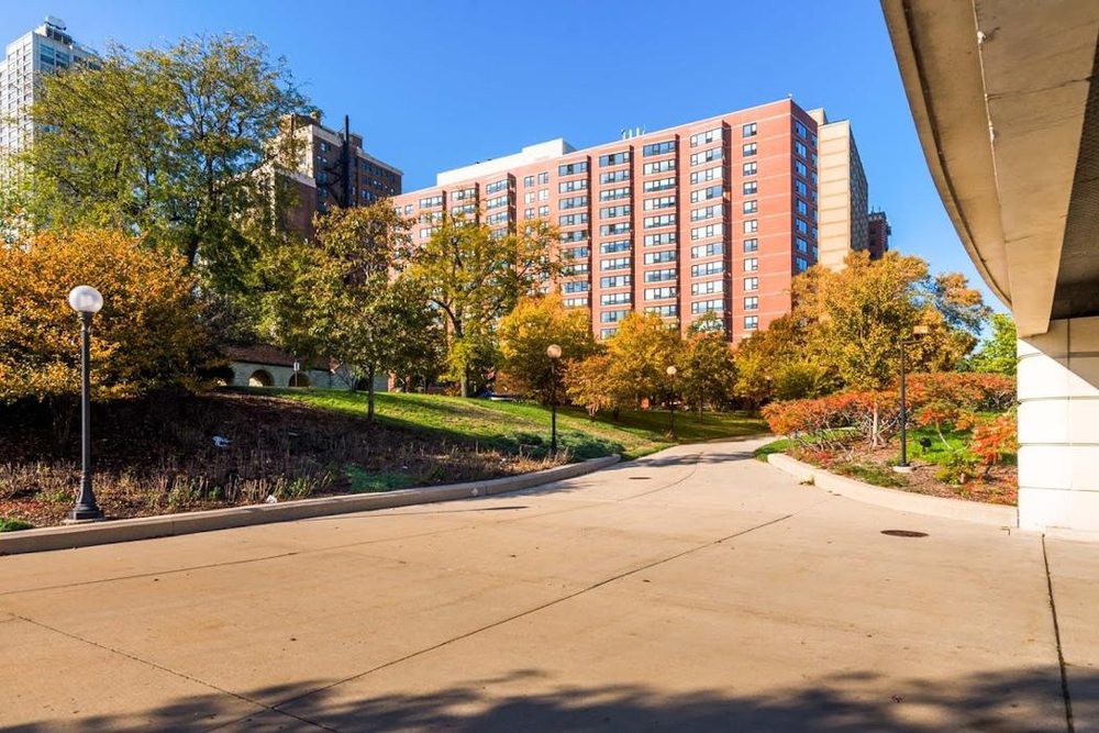A tall apartment building surrounded by autumn trees and a pathway in an urban setting.