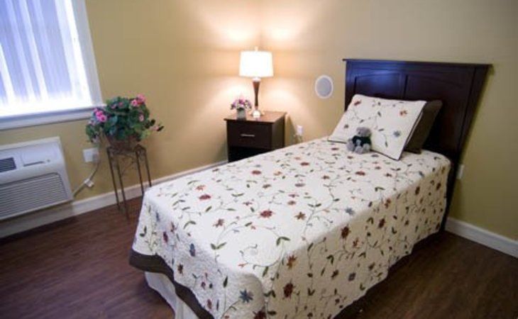 A cozy bedroom with a single bed adorned with a floral quilt, a nightstand featuring a lamp and decor.