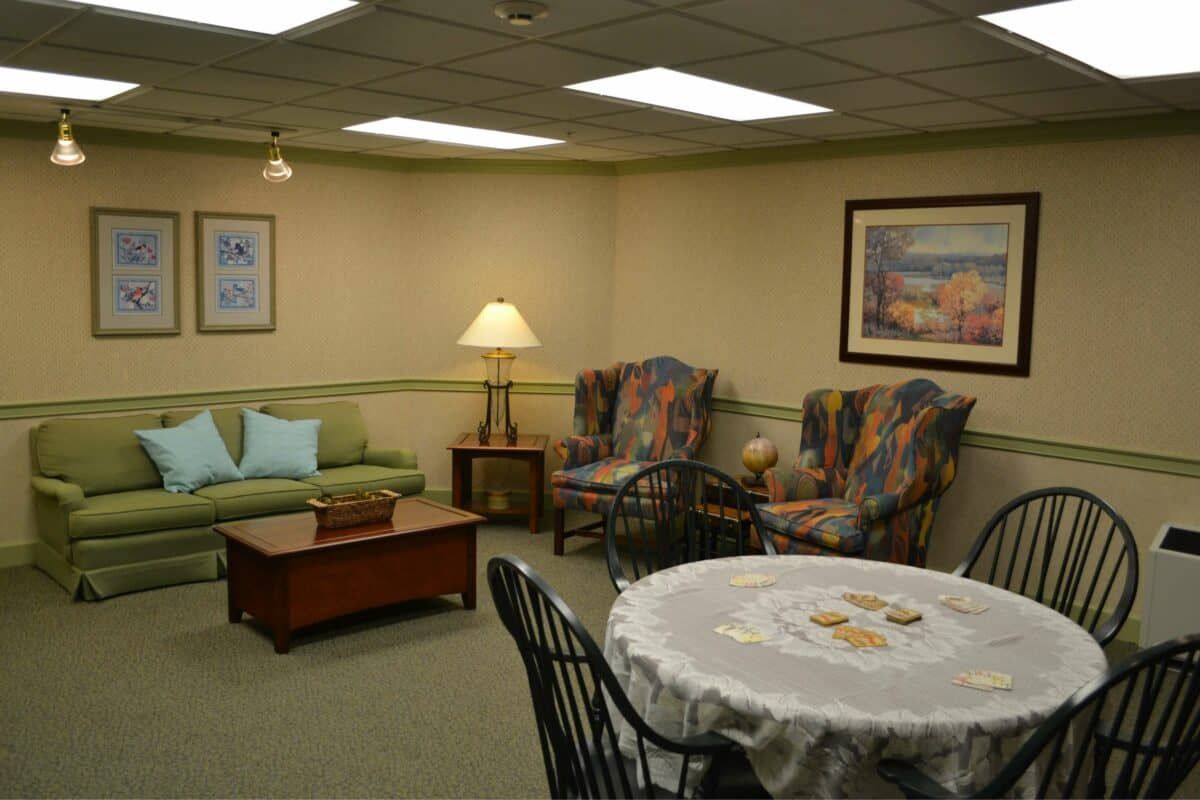 A cozy living room with a sofa, patterned chairs, a lamp, and a table adorned with a lace cloth.
