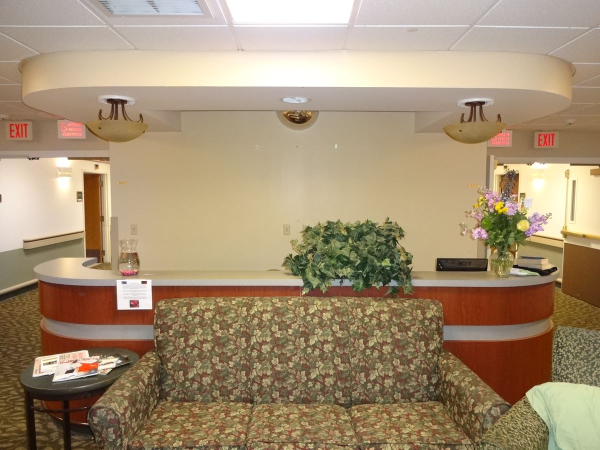 A waiting room with a floral-patterned couch, plants, and a reception desk in the background.
