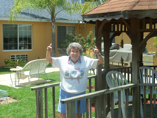 An elderly woman joyfully posing with her hands up in a sunny garden.