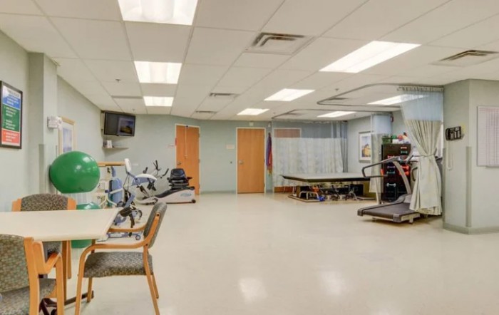 A spacious rehabilitation room equipped with various exercise machines and therapy tables.