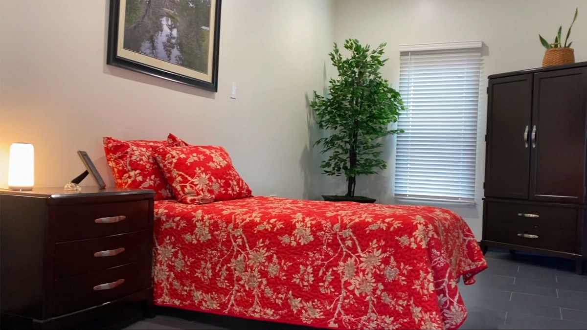 A cozy bedroom with red floral bedding and a potted plant near the window.