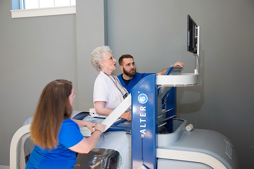 An elderly woman engaged in a rehabilitation session, assisted by two healthcare professionals using advanced technology.