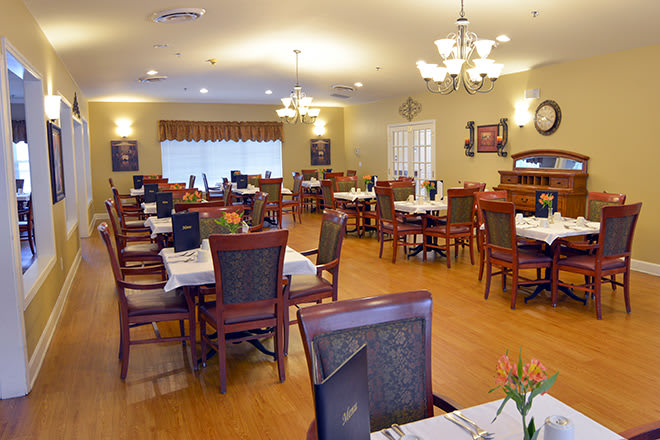 A spacious dining area with neatly arranged tables and chairs, illuminated by chandeliers.