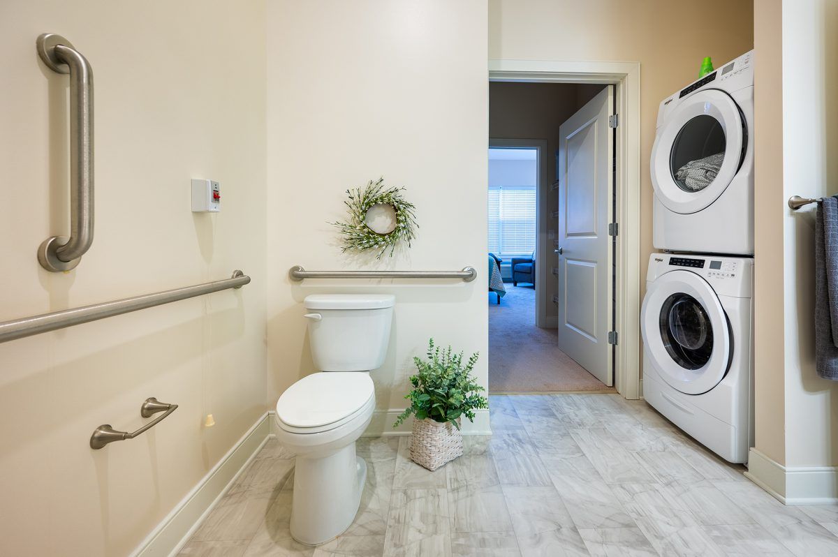 A bathroom with a toilet and adjacent laundry area featuring a washer and dryer, decorated with plants and wall decor.