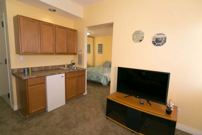 Cozy apartment living area with kitchen and TV setup, leading into a bedroom.