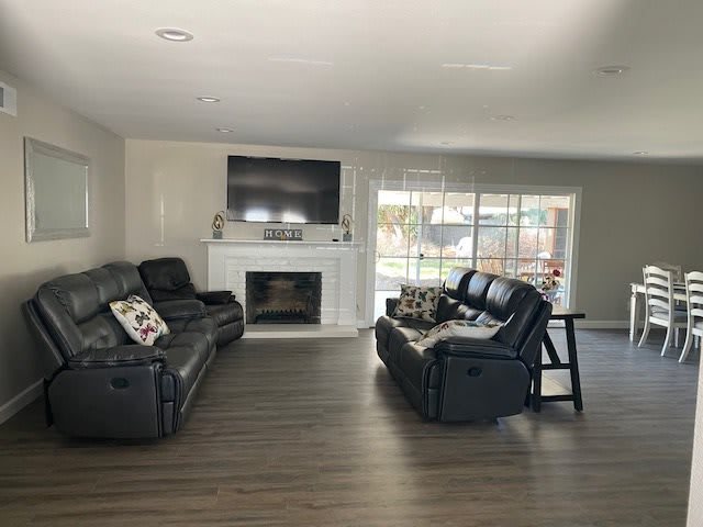 A modern living room with black sofas, a television above a fireplace, and hardwood flooring.