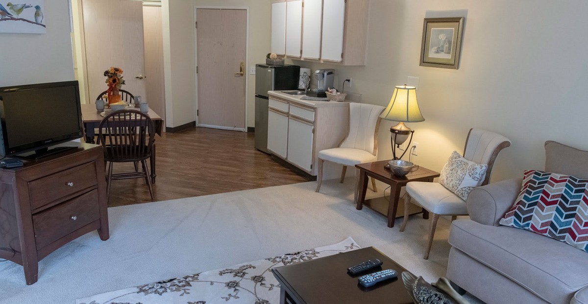 A cozy apartment living area with a kitchenette, featuring furniture and a warm lamp.