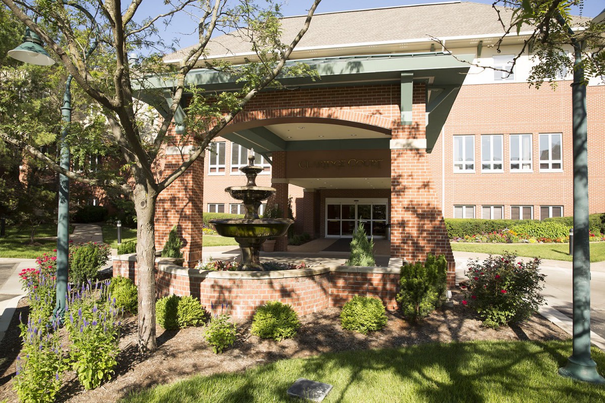 A sunny view of a building entrance with a fountain and landscaped garden.