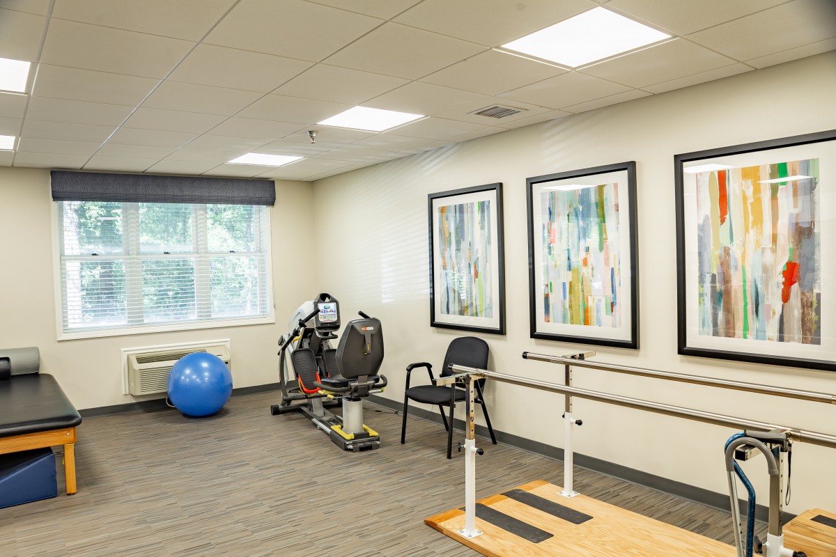 A rehabilitation room equipped with exercise machines, an exercise ball, and parallel bars.