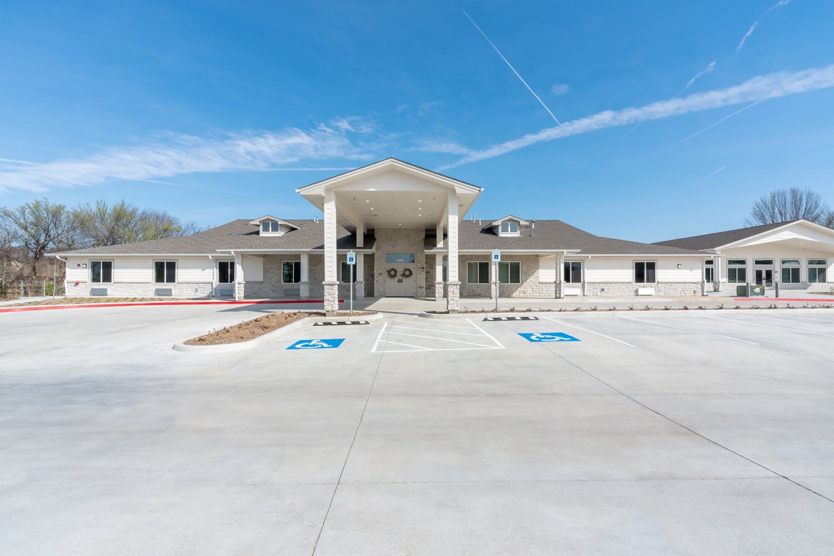 A modern building with columns at the entrance, featuring a spacious parking lot and clear blue sky.