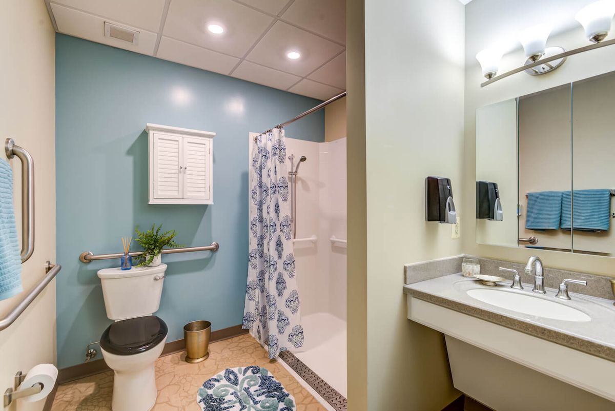 A modern bathroom featuring a shower with a patterned curtain, a toilet, and a sink with a mirror.