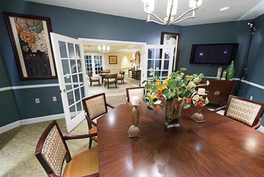 Elegant dining room with a wooden table and floral centerpiece, leading to an adjacent room through open French doors.