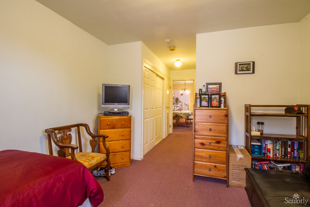A cozy bedroom with wooden furniture, a TV, and a view into a hallway.