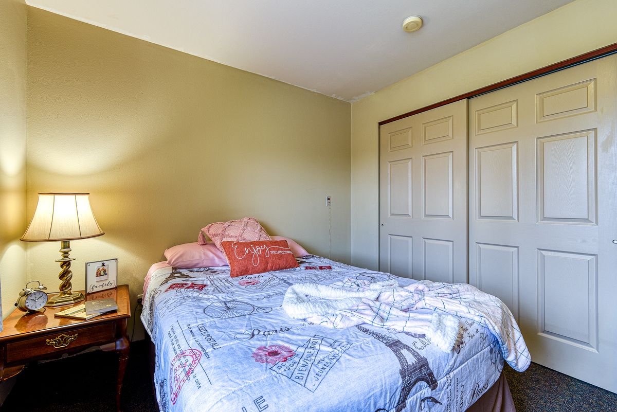 A cozy bedroom featuring a neatly made bed with patterned linens, a nightstand with a lamp, and a closed closet.