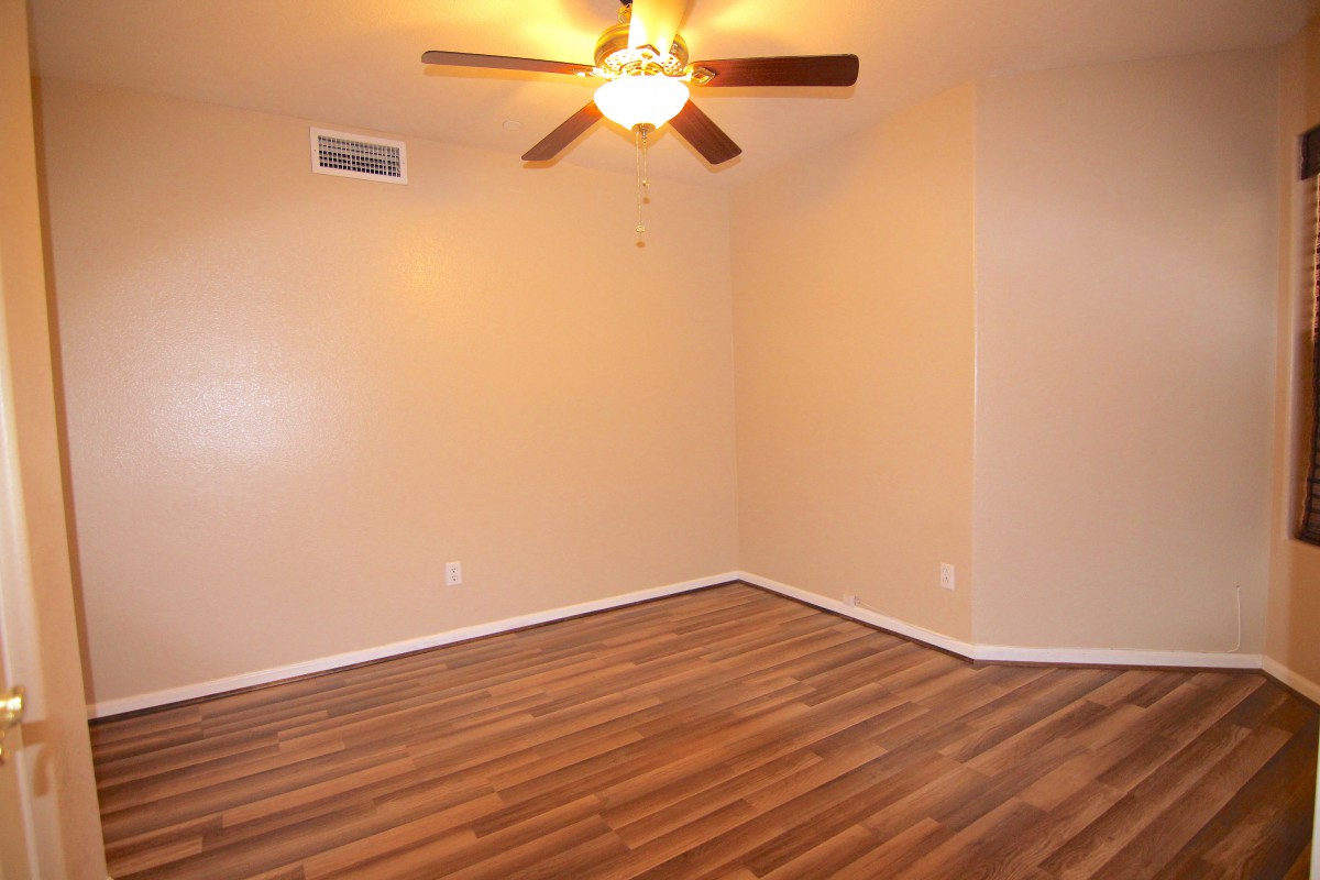 An empty room featuring a ceiling fan and wood flooring with beige walls.