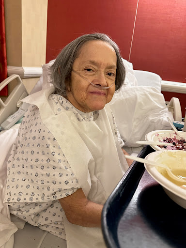 An elderly woman in a hospital bed enjoying her meal.