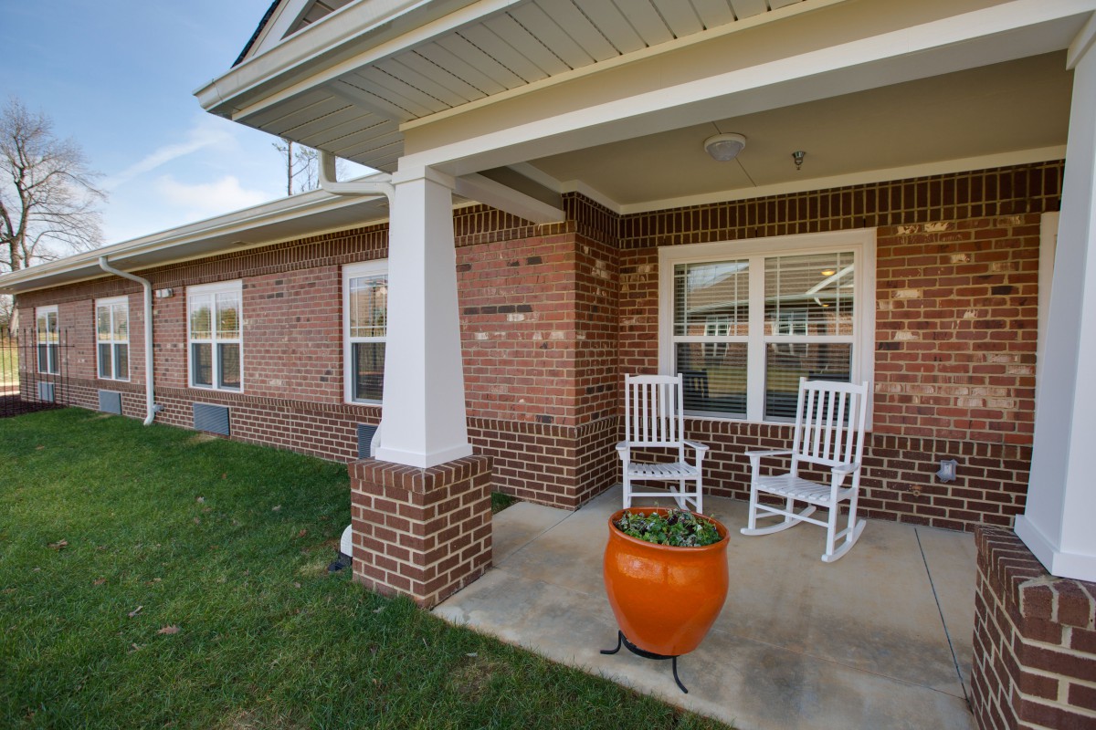 A cozy brick porch with two white rocking chairs and an orange planter.