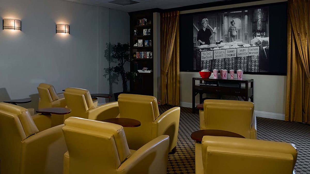 A cozy home theater with yellow chairs facing a large screen displaying a black and white movie.
