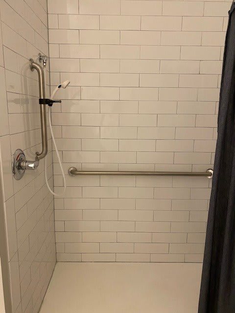 A tiled shower with a grab bar and handheld showerhead.