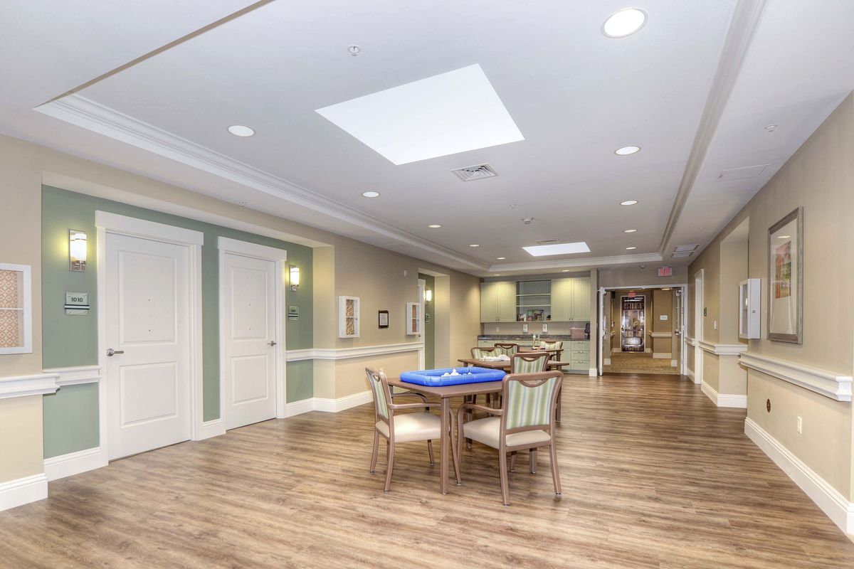 A spacious indoor lounge area with a table and chairs, featuring hardwood flooring and ceiling lights.