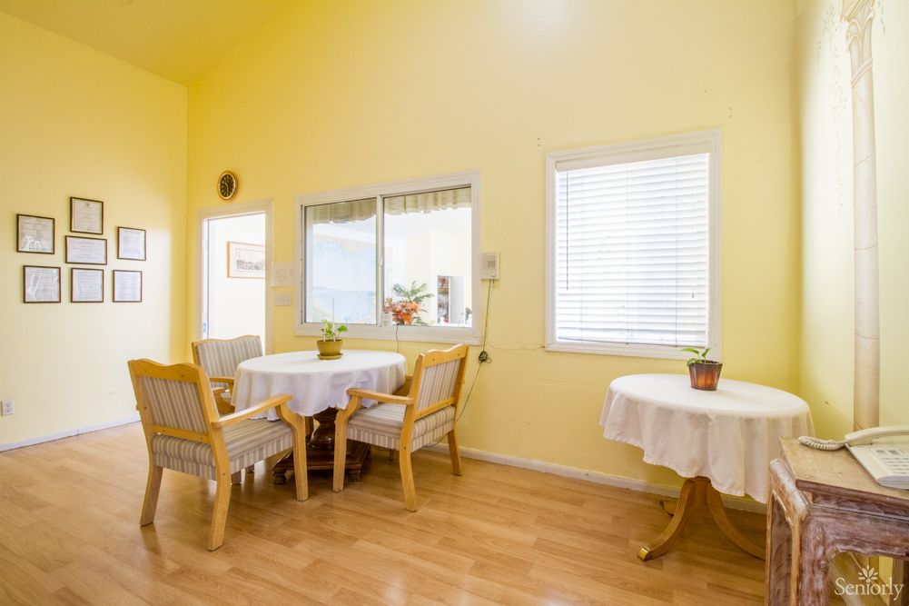 A bright dining area with yellow walls, featuring tables and chairs, decorated with small plants near the windows.