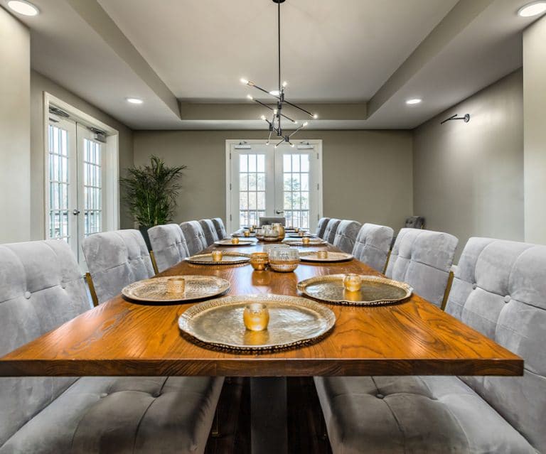 A stylish dining room with a large wooden table set for a meal and surrounded by plush chairs.