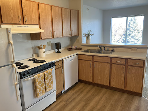 A modern kitchen featuring wooden cabinets and essential appliances, illuminated by natural light.