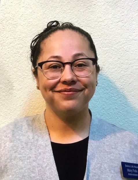 A woman wearing glasses is smiling in a portrait-style photo.