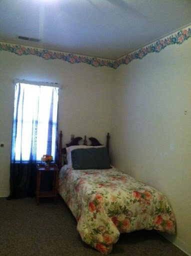 A cozy bedroom with floral bedding, a nightstand, and a window letting in natural light.